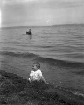 [McDonald?] baby sitting at edge of water on beach